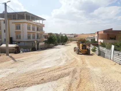 Diyarbakır parke kilit taşı ve kaldırım imalatı şantiyesinde, kazısı biten zemine dökülen alttemel malzemesinin greyder iş makinesi ile hassas kot ayarıyla serilmesi ve tesviye edilmesi